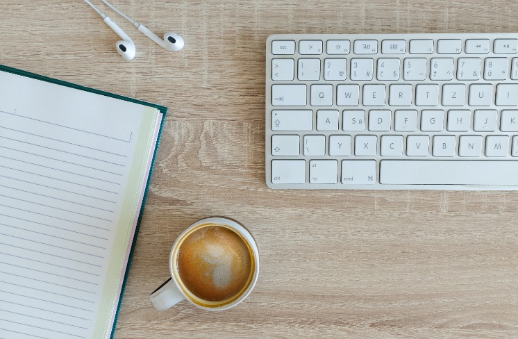 Keyboard, coffee mug, earphones and notebook on a desk